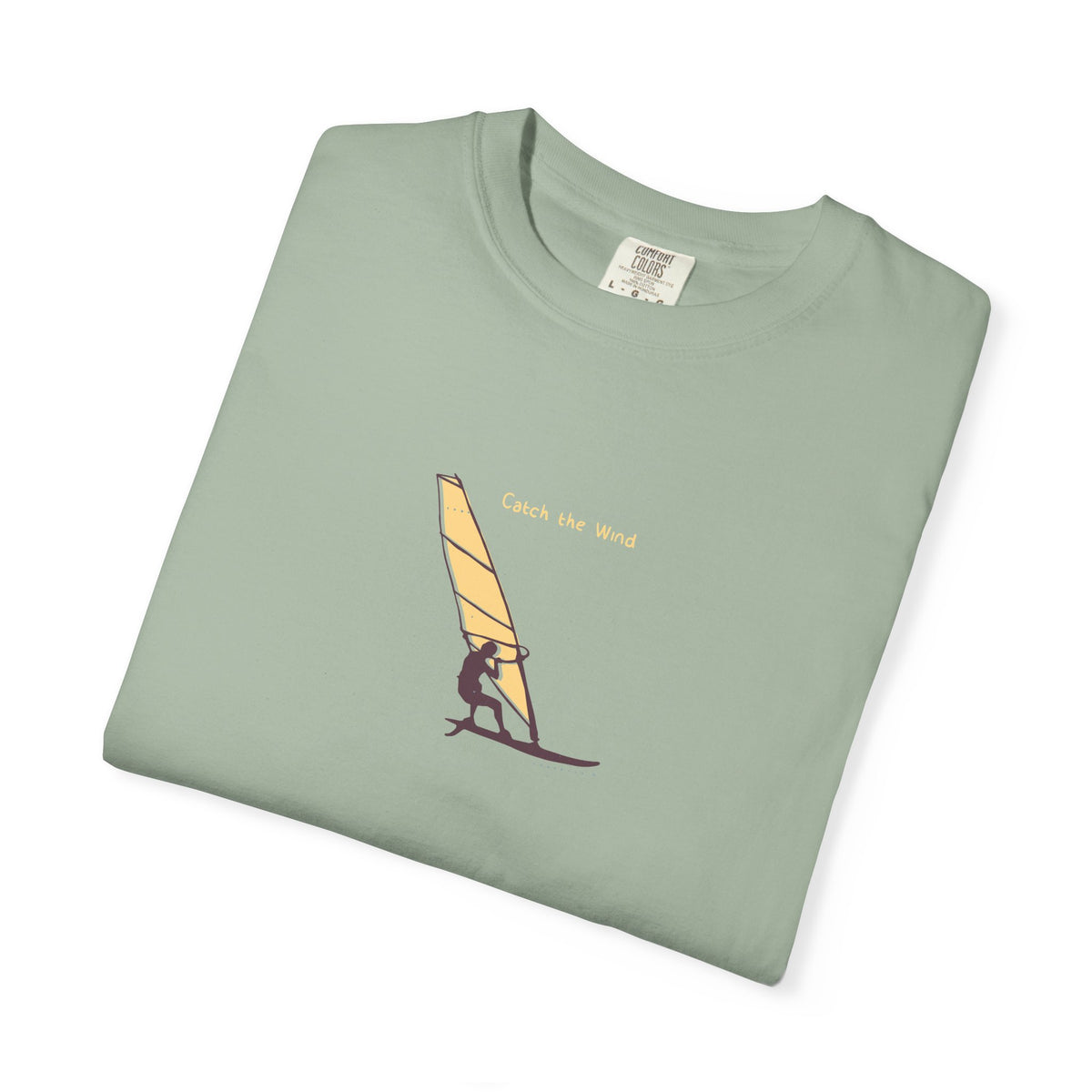 Folded green t-shirt with a windsurfing design and 'Catch the Wind' text on a white background