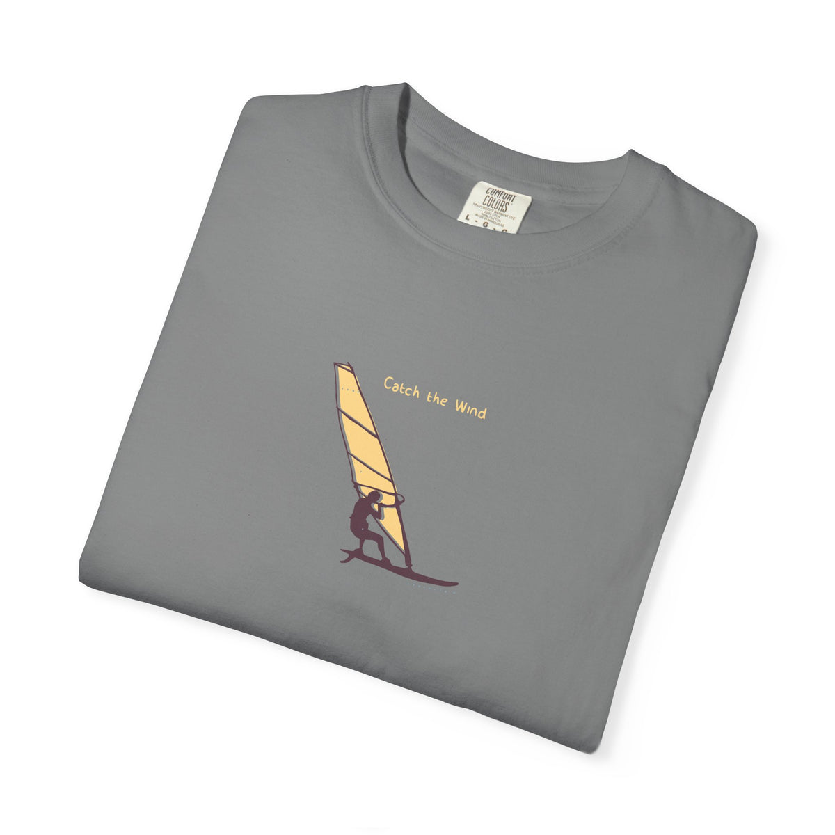 Folded gray t-shirt with a graphic of a person on a windsurf board and 'Catch the Wind' text.